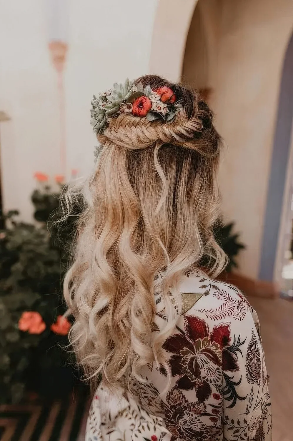Boho wedding hairstyle with a fishtail braid halo, waves down and bold blooms and pale leaves tucked in.