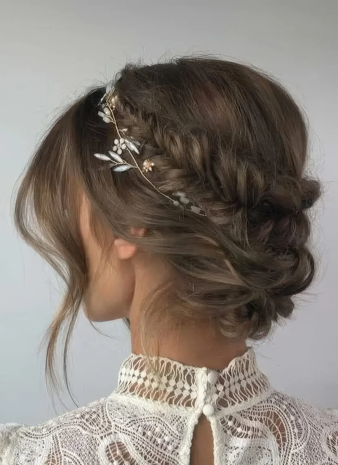 Updo with a fishtail braided halo, a low bun and face-framing locks plus a hair vine accenting the hairstyle.