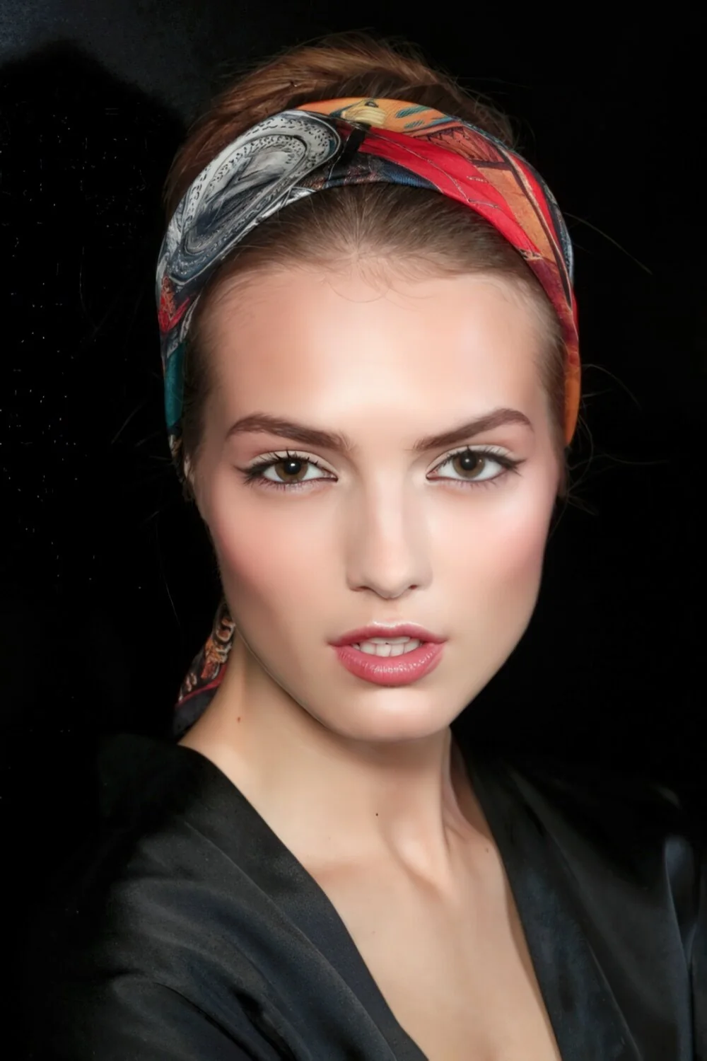 Bangs tucked under a knotted headscarf.