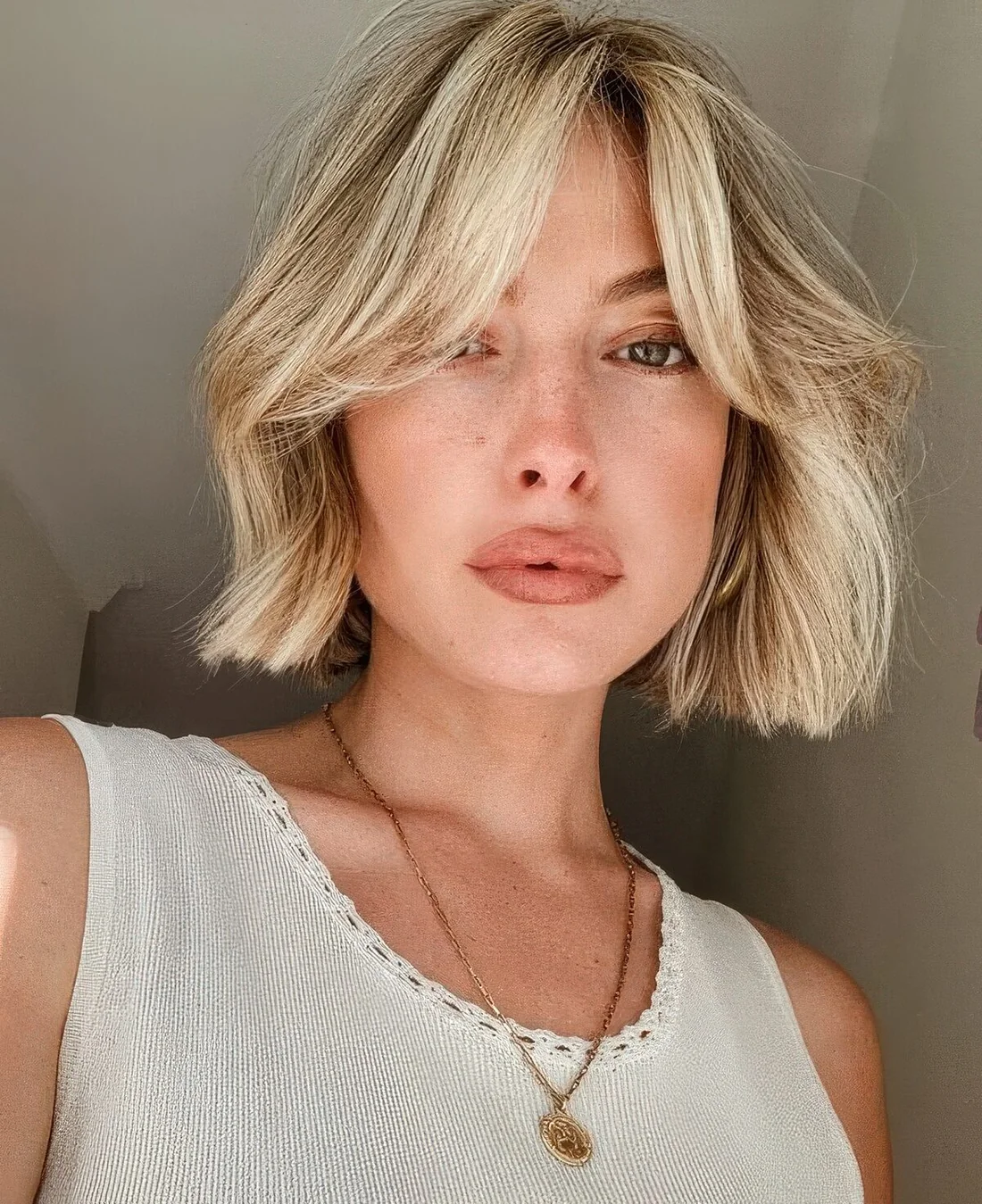Blonde 90s chin-length haircut with curtain bangs and some volume.
