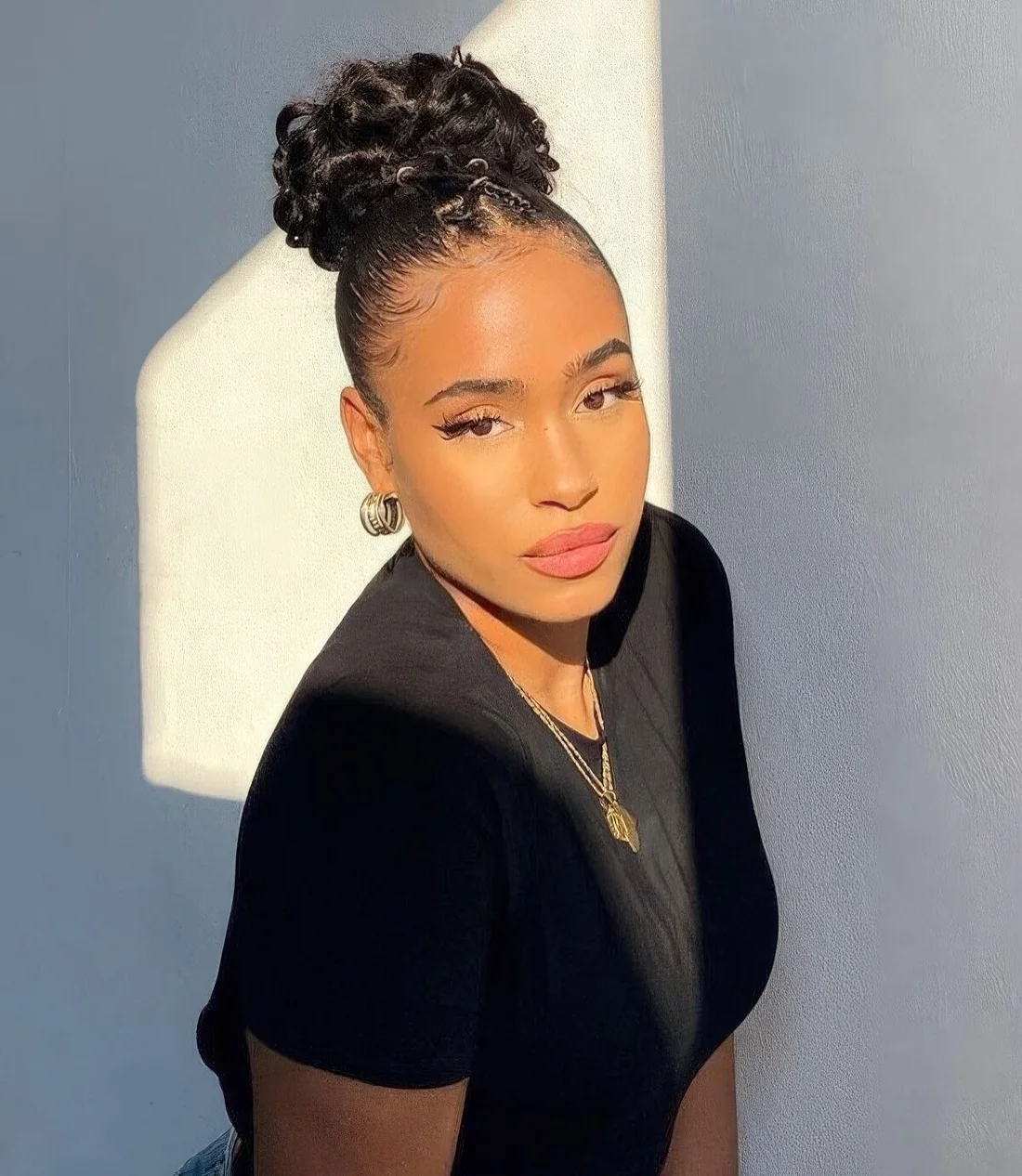 Slick your hair back into a high bun, leaving two small sections of hair for braiding, create two braids, cross them, and pin them back near the bun.