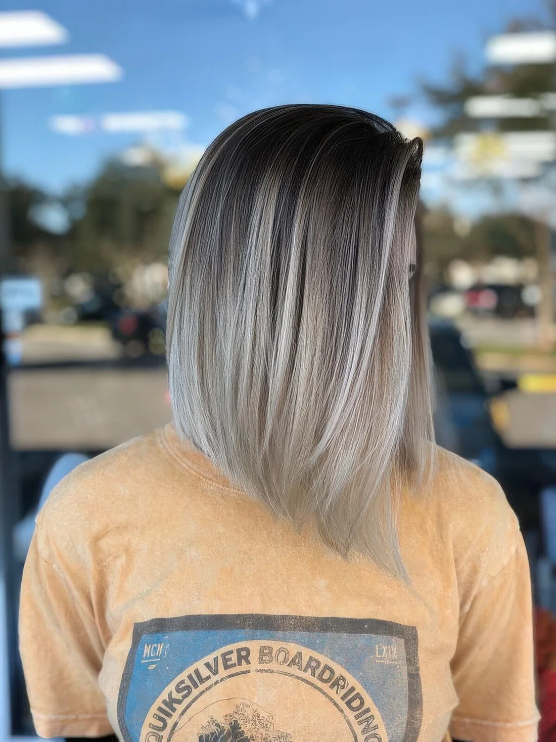 Long angled blonde bob with blonde balayage and slightly curled ends.