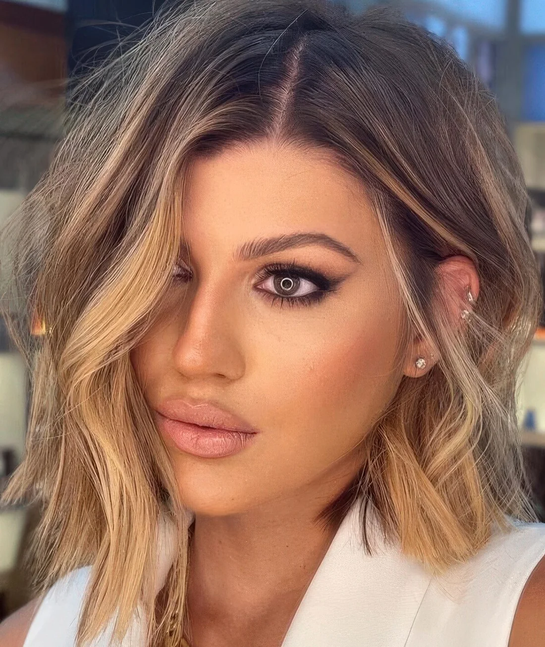 Chic asymmetrical long bob with honey blonde balayage and messy waves.