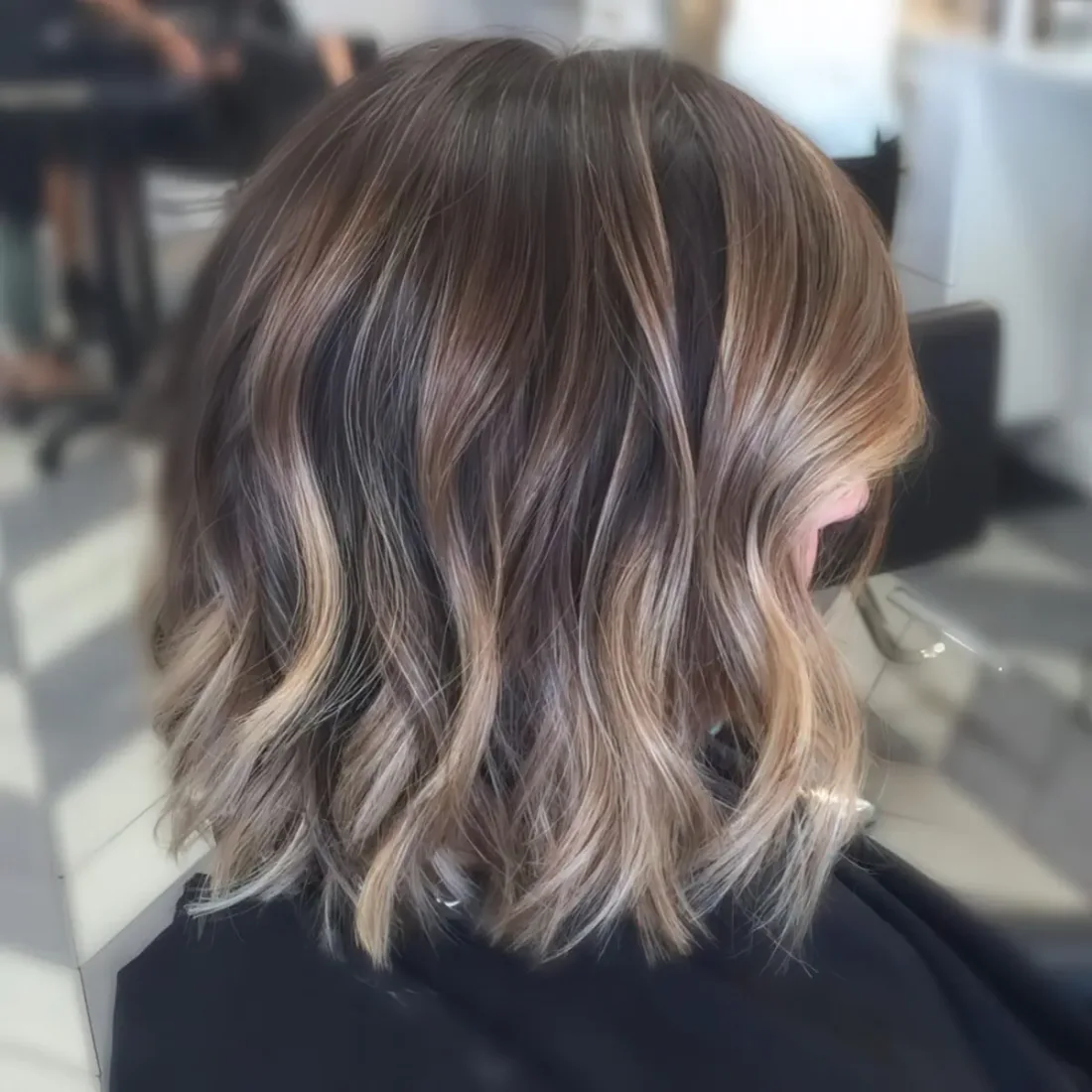 Short brunette hair with gold balayage and light waves.
