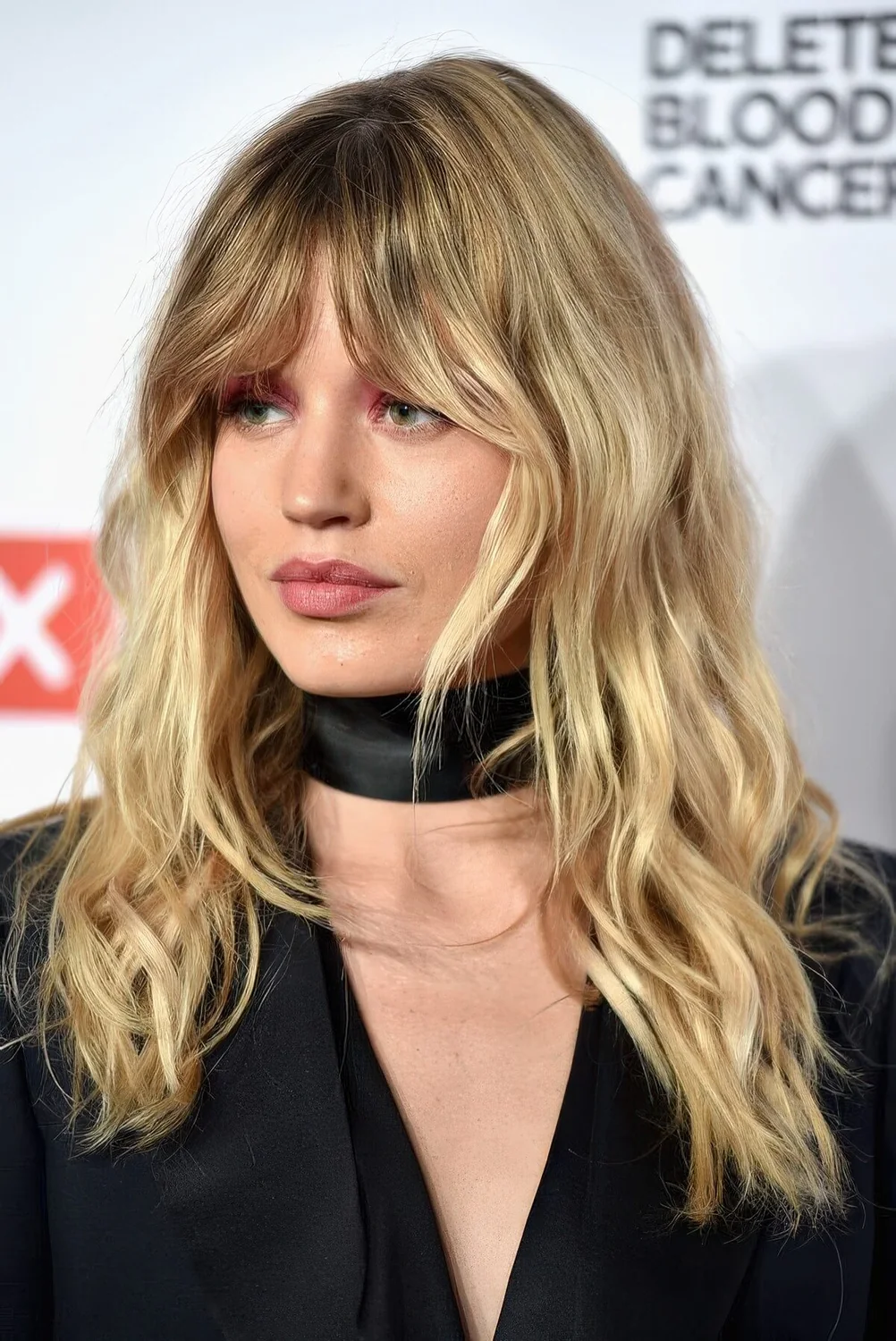 Wavy blonde hairstyle with a darker root and Bardot bangs.