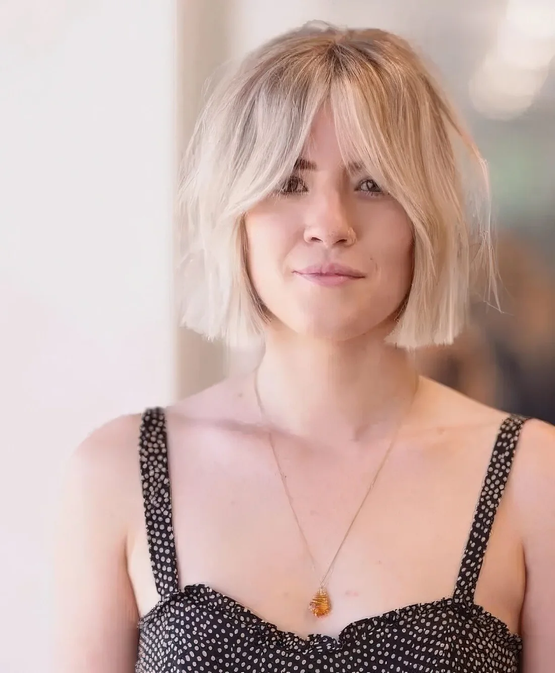 Chin-length icy blonde bob with center part and Bardot bangs.