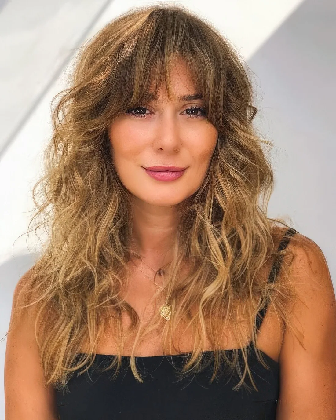 Long wavy hair with gold blonde balayage and messy Bardot bangs.