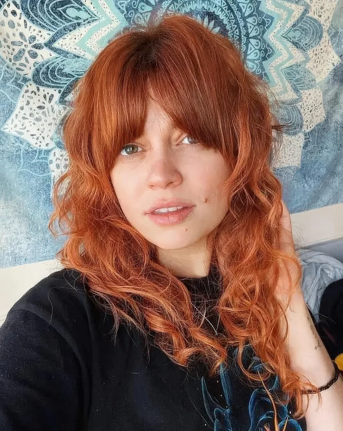 Curly ginger hair with Bardot curtain bangs.