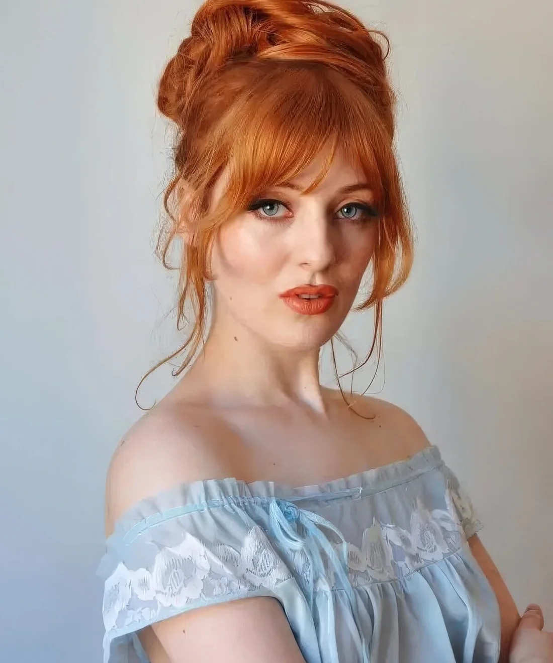 Bright ginger hair in a top knot, with some face-framing hair and lovely Bardot bangs.