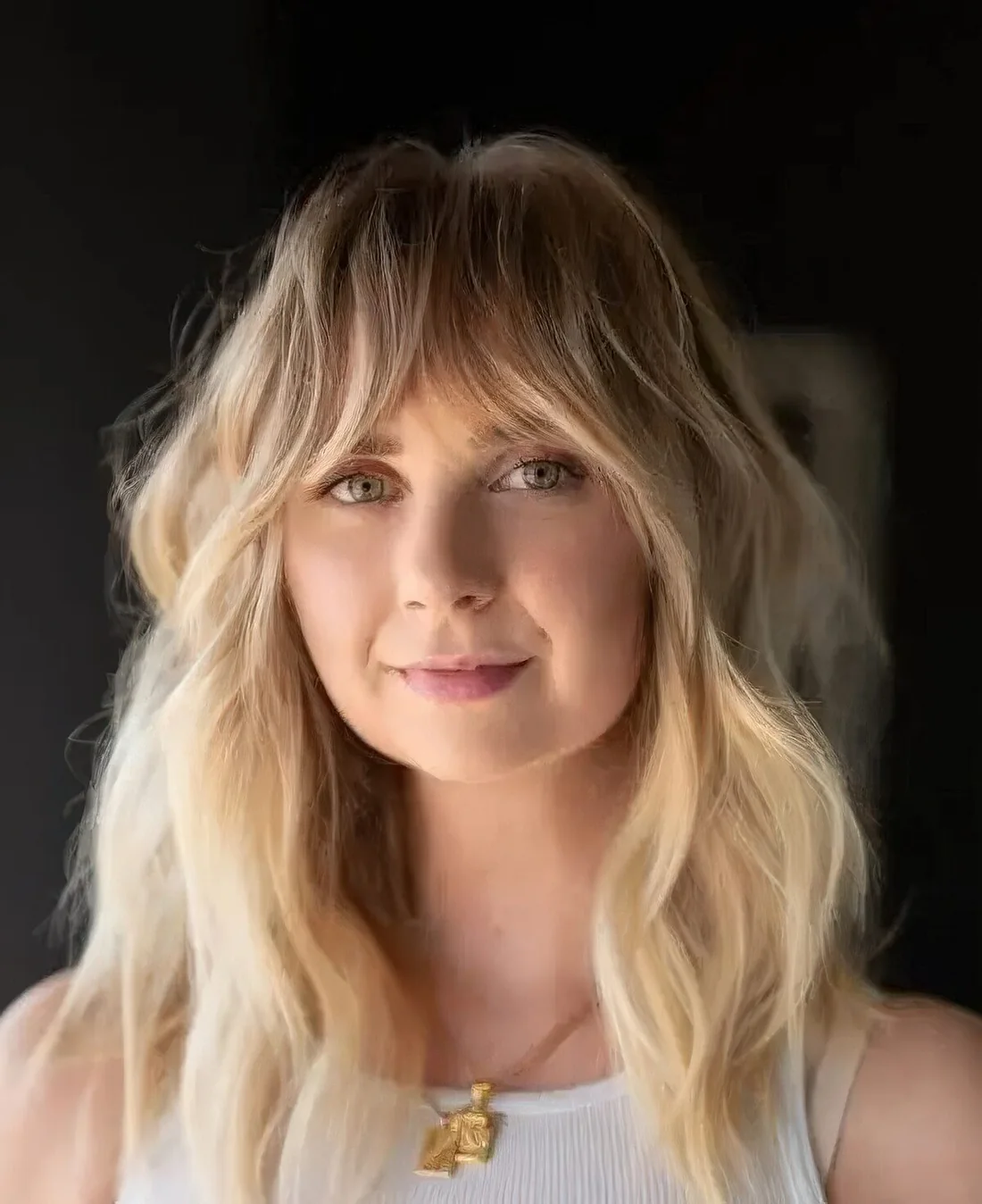 Long blonde wavy hair with a lot of volume and texture and Bardot bangs.