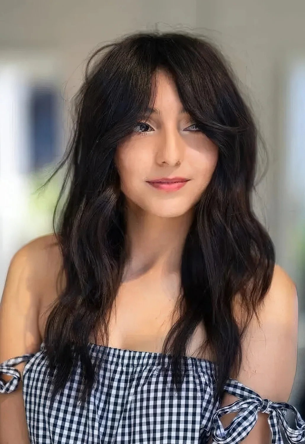 Long dark hair with waves and texture, with center part and Bardot bangs.