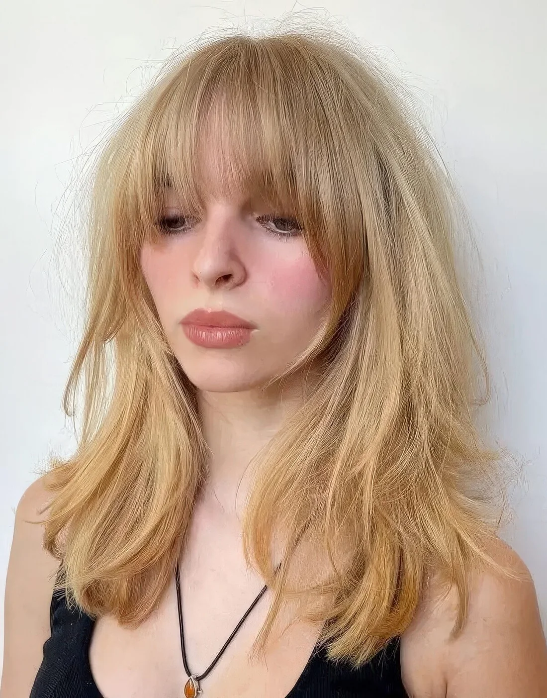 Long golden blonde hair with layers and long and expended Bardot bangs.
