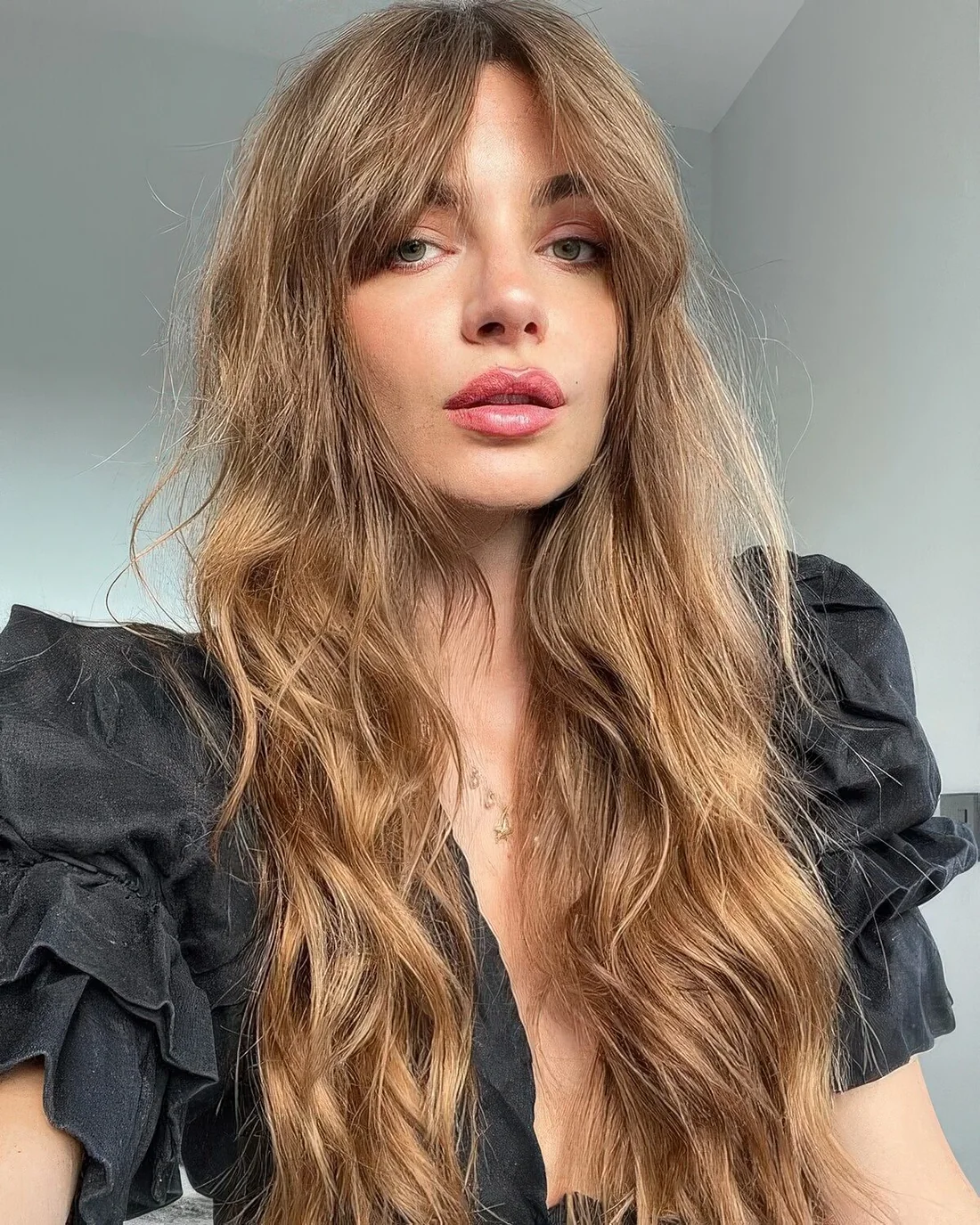 Long light brunette hair with waves and classic Bardot bangs.
