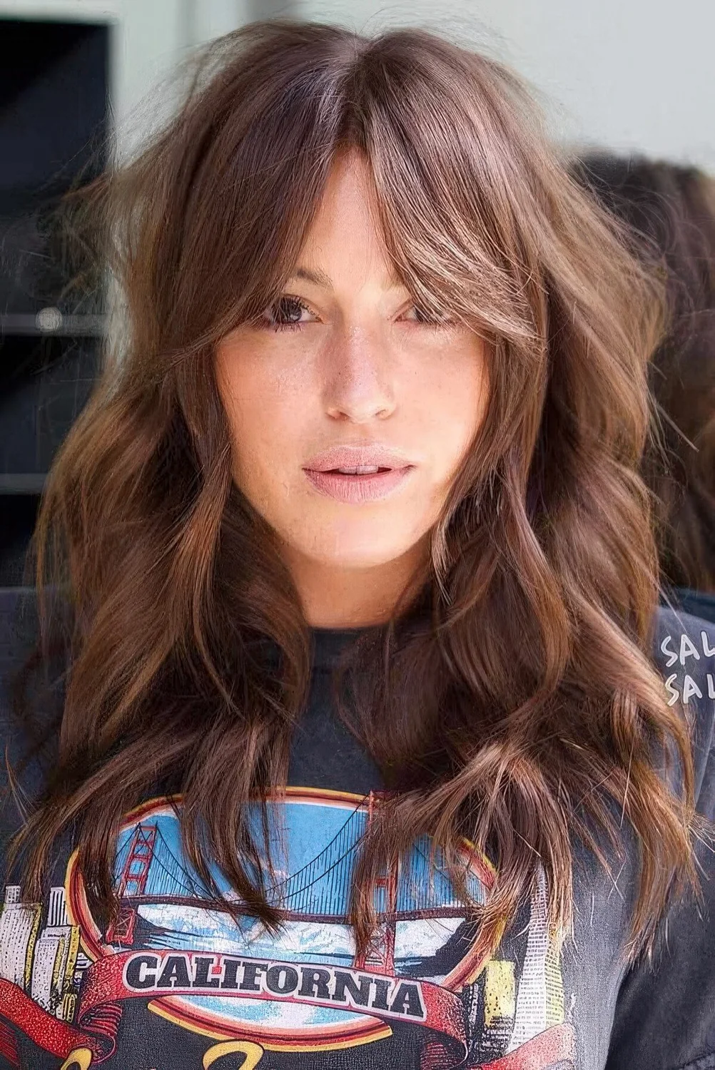 Long wavy brown hair cut in layers and with a Bardot fringe.