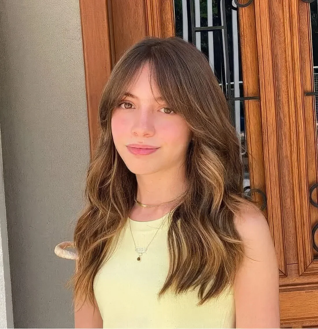 Long wavy hair with blonde highlights, center parting and Bardot curtain bangs.