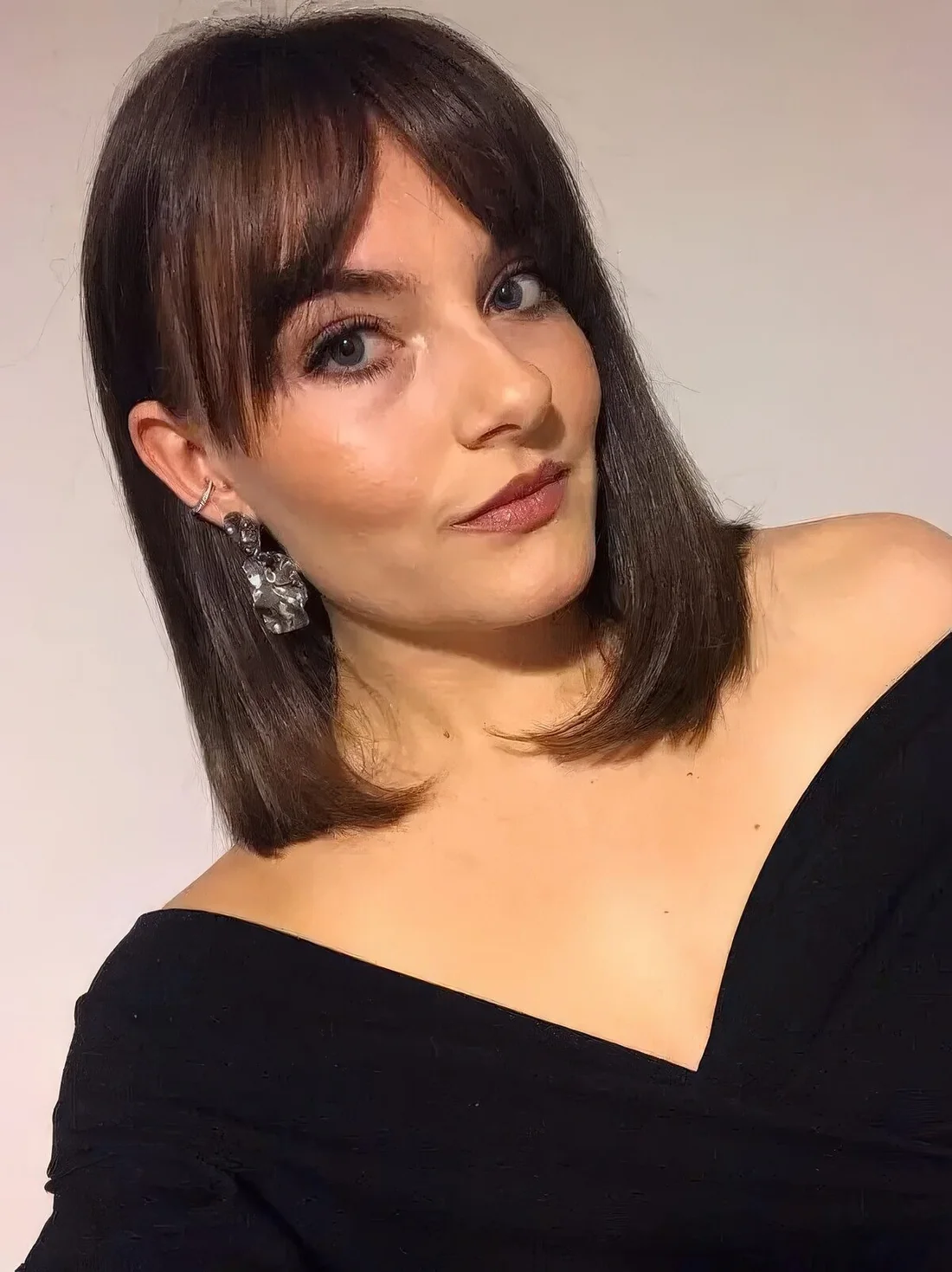 Shoulder-length dark brunette hair with Bardot bangs and center parting.