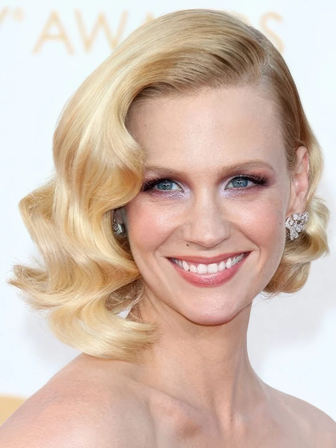 Glam golden blonde baroque style with curls and a deep side part.