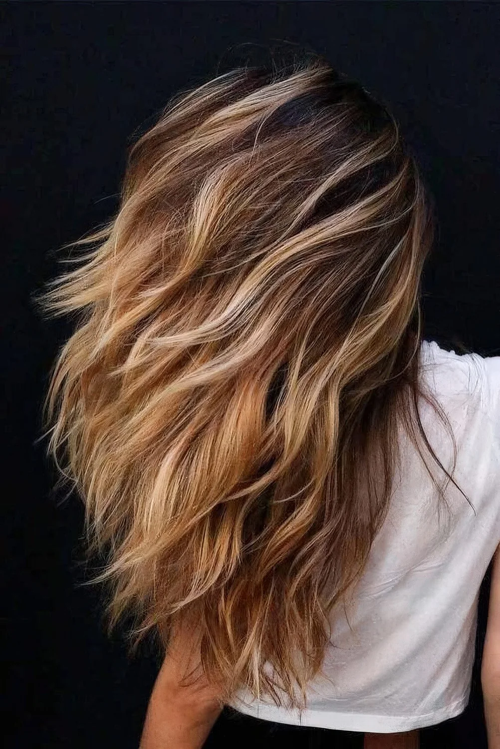 Long and dimensional brunette hair with blonde balayage and beach waves.
