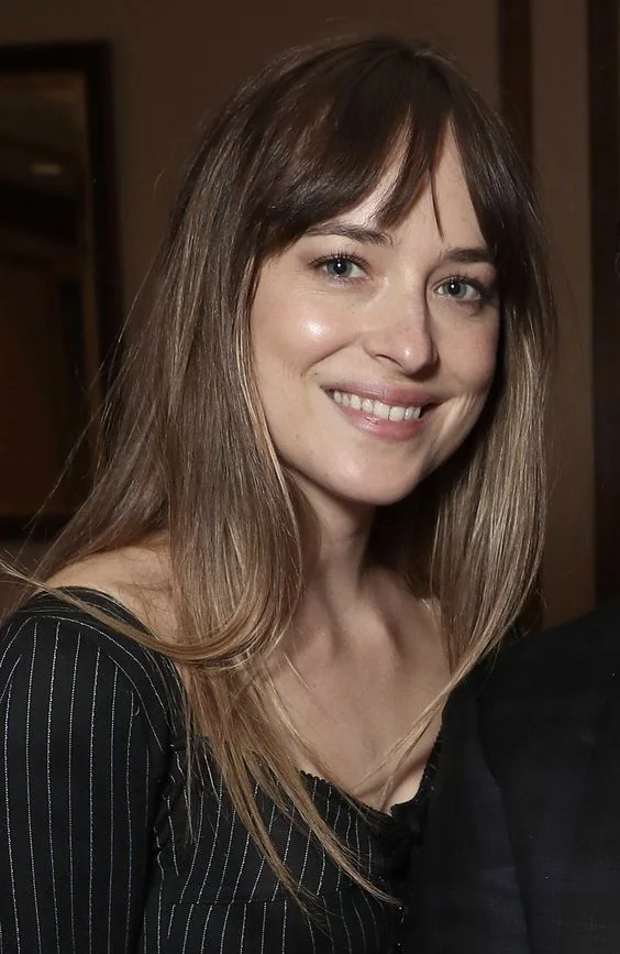 Dakota Johnson rocking long brown hair with an ombre effect and wispy Birkin bangs.