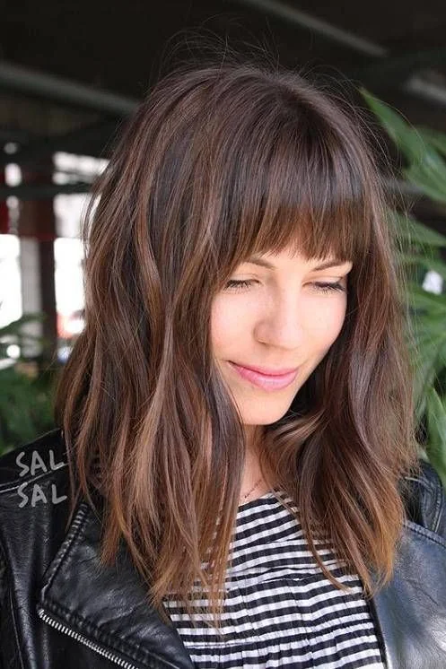 Dark brown hair with alighter chestnut balayage, messy waves and Birkin bangs wispy ones.