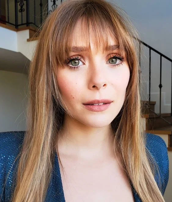 Elizabeth Olsen wearing long honey blonde hair with blonde balayage and wispy overgrown Birkin bangs.