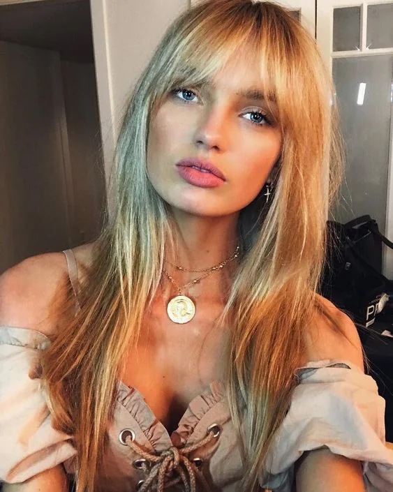 Long blonde hair with balayage and a darker root, with effortlessly chic Birkin bangs.