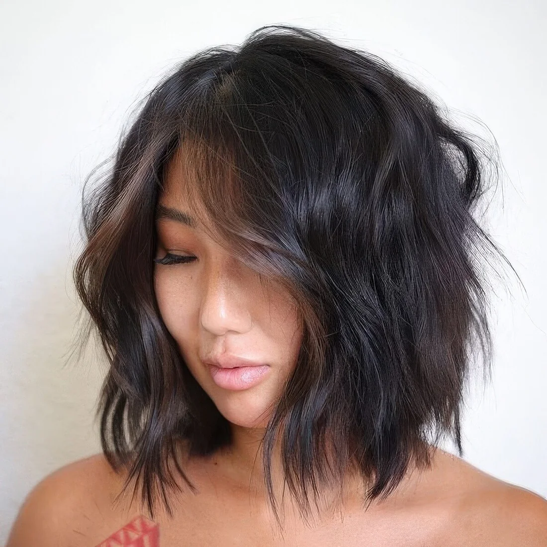 Black shaggy long bob with messy waves and chestnut money piece.