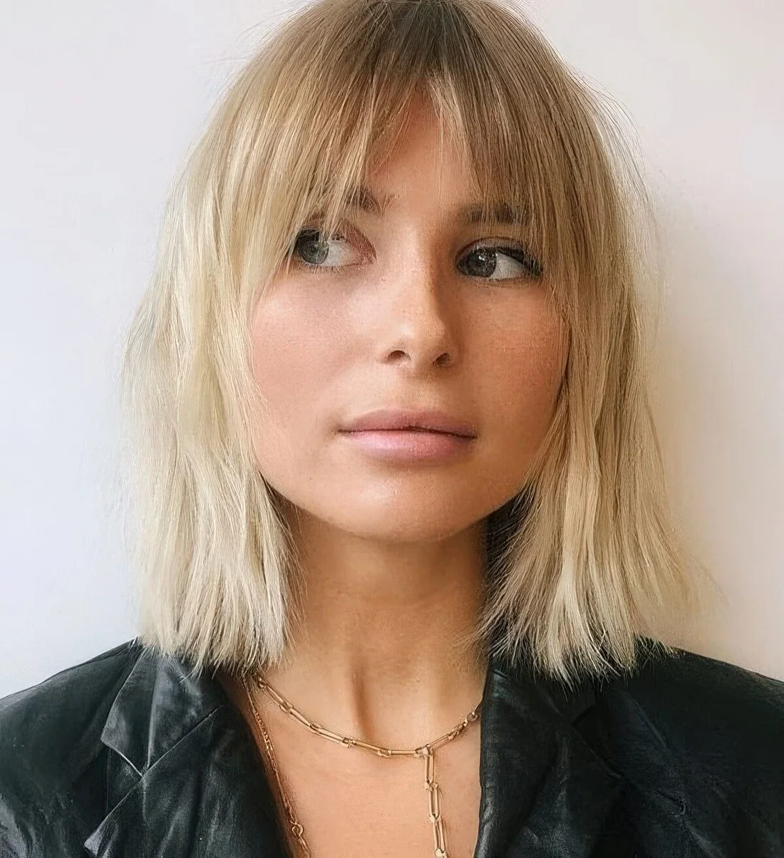 Chic long blonde bob with a darker root and curtain and bottleneck bangs.