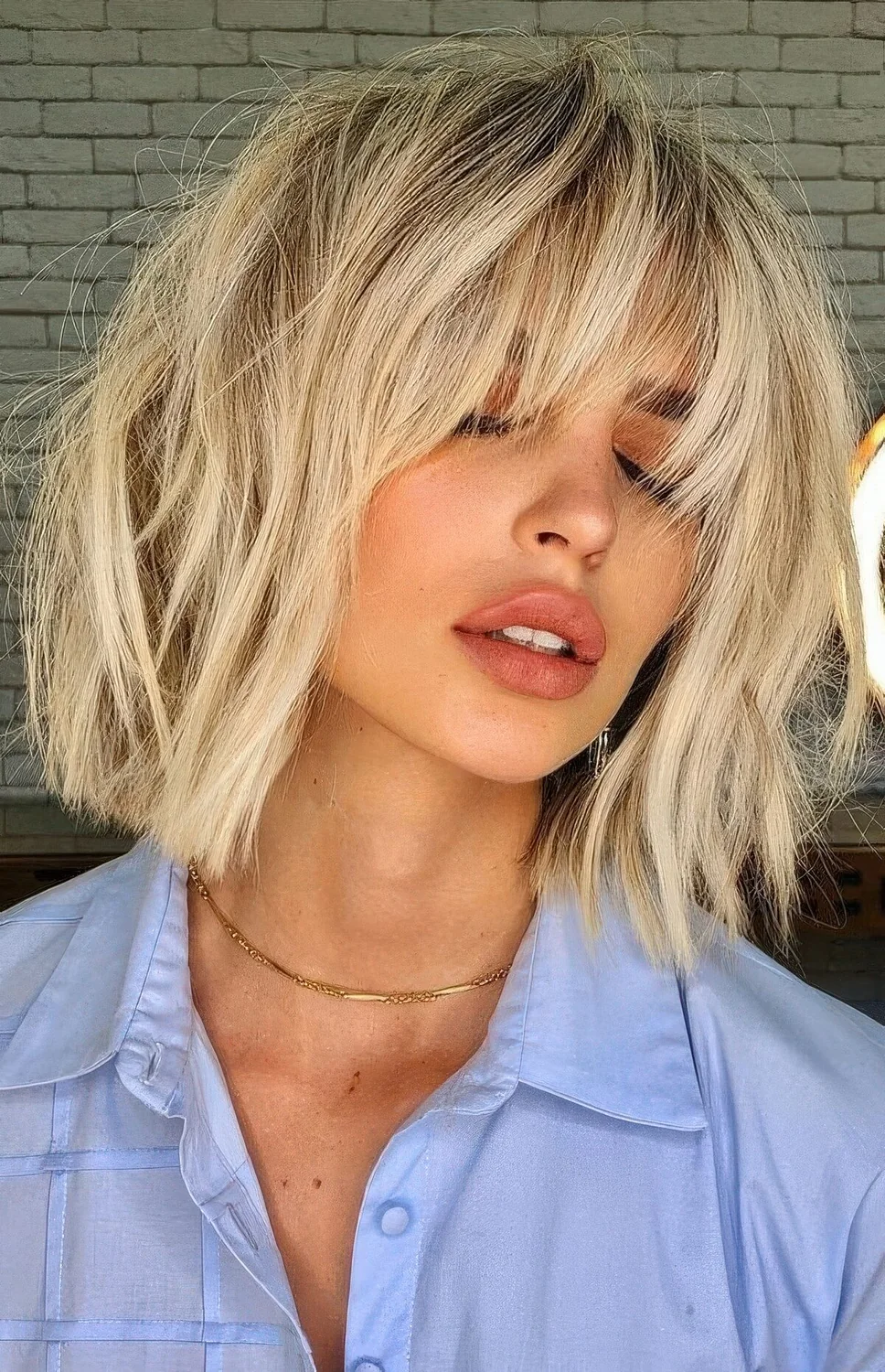 Long bob haircut of cool vanilla tone and with bangs and messy waves.