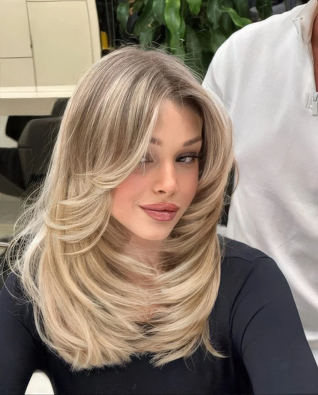 Blonde butterfly haircut with a darker root, a lot of volume and wavy ends.