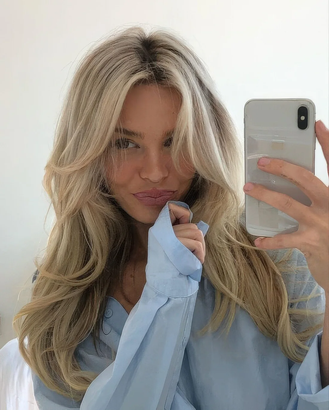 Bleached blonde butterfly haircut on long hair, with a darker root, wavy ends and a bit of volume.