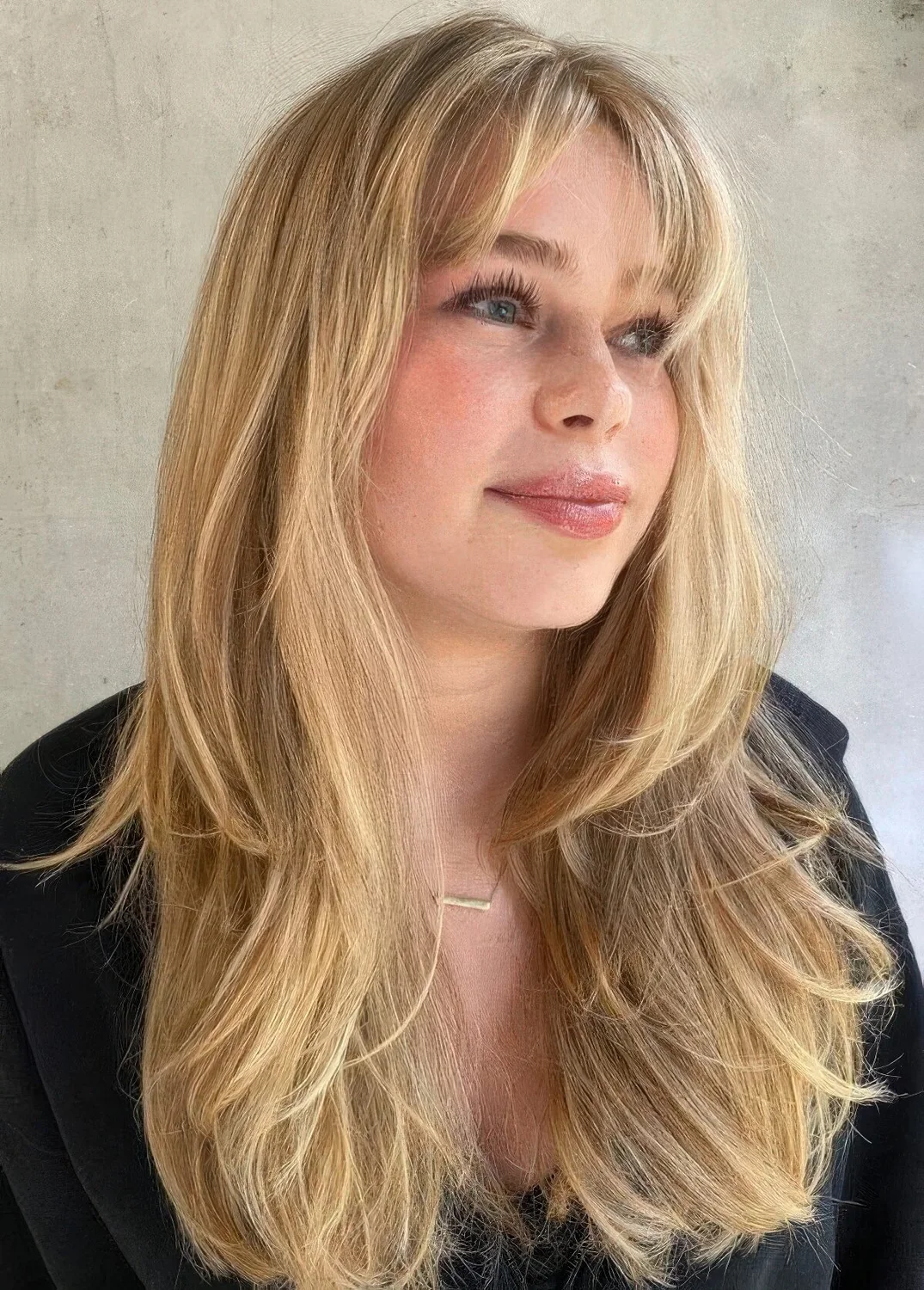 Textural and dimensional blonde butterfly haircut with curtain bangs and volume.