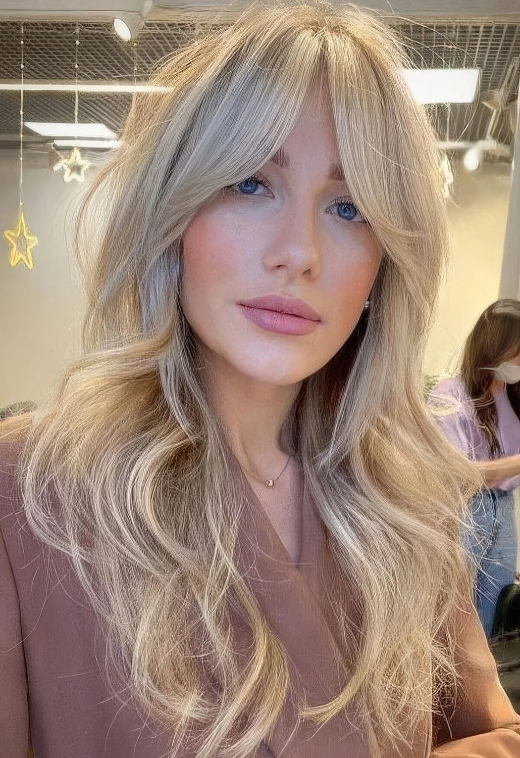 Long blonde butterfly haircut with curtain bangs and waves.