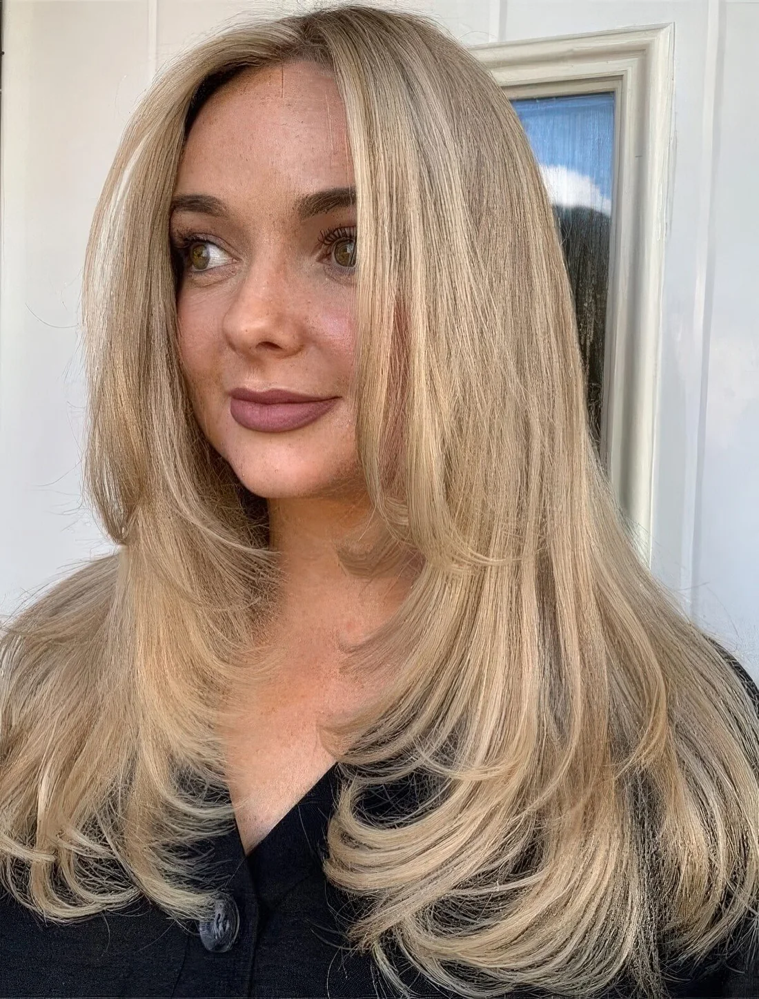 Long blonde butterfly haircut with long curtain bangs, curved ends and a bit of volume.