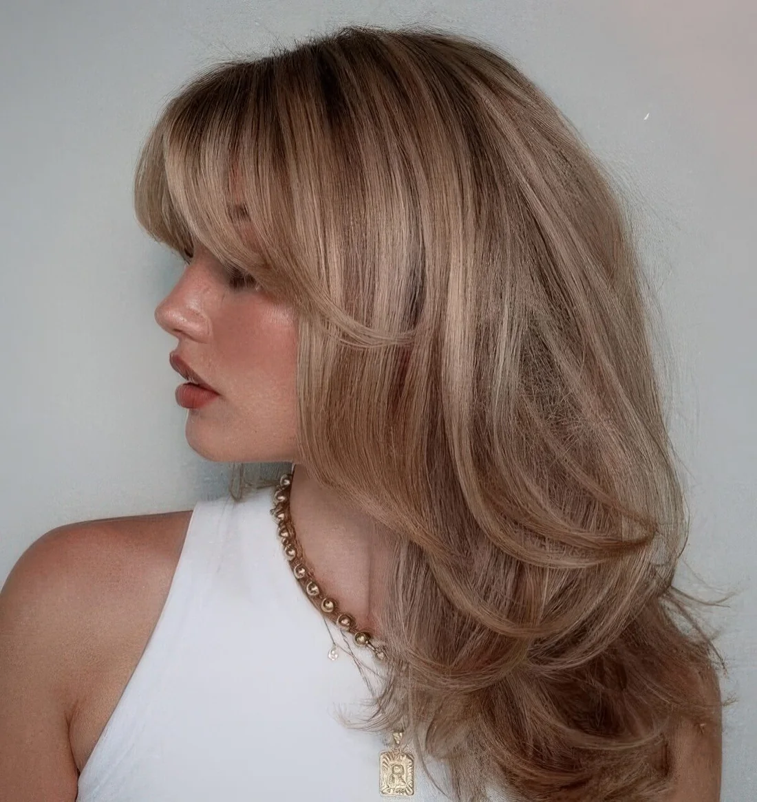 Blonde butterfly haircut with highlights and side and bottleneck bangs.