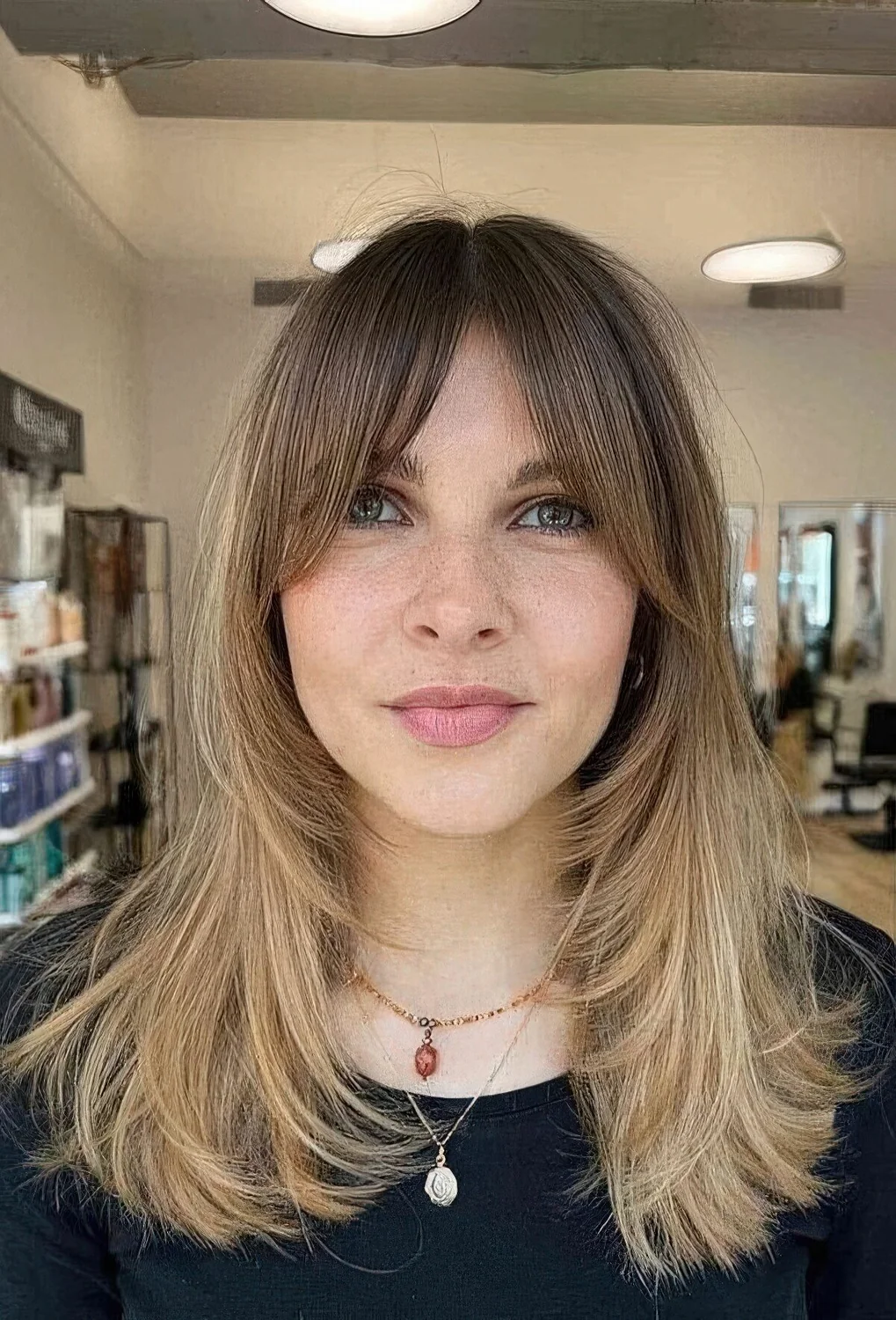 Medium blonde butterfly haircut with a darker root and front plus bottleneck bangs.