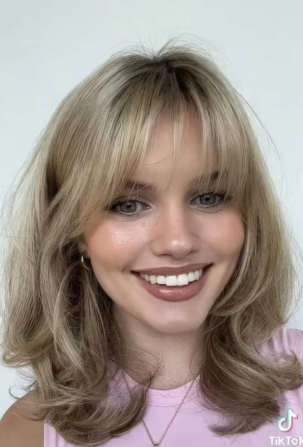 Medium blonde butterfly haircut with wispy bangs and waves.