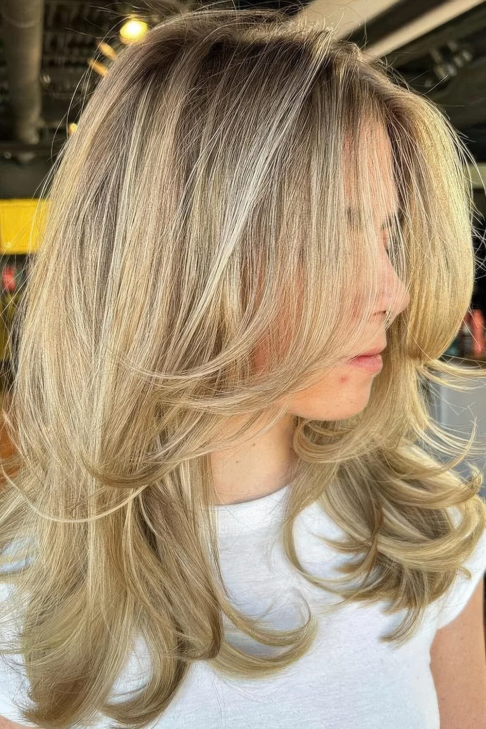Medium-length blonde butterfly haircut with curled ends, a bit of volume and a darker root.