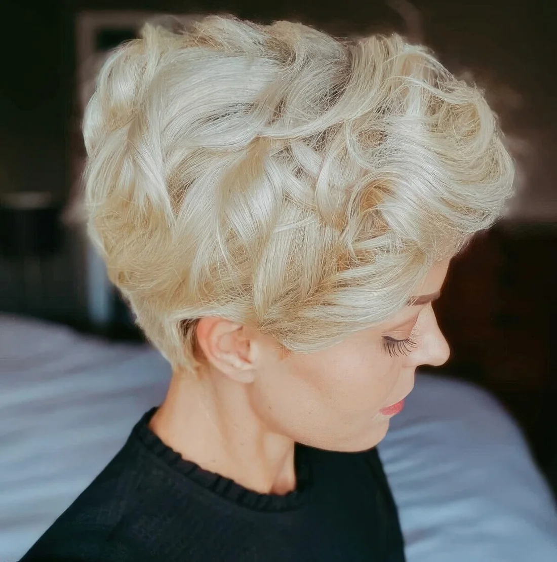 Layered blonde wavy pixie haircut with the right texture and a deep side part.