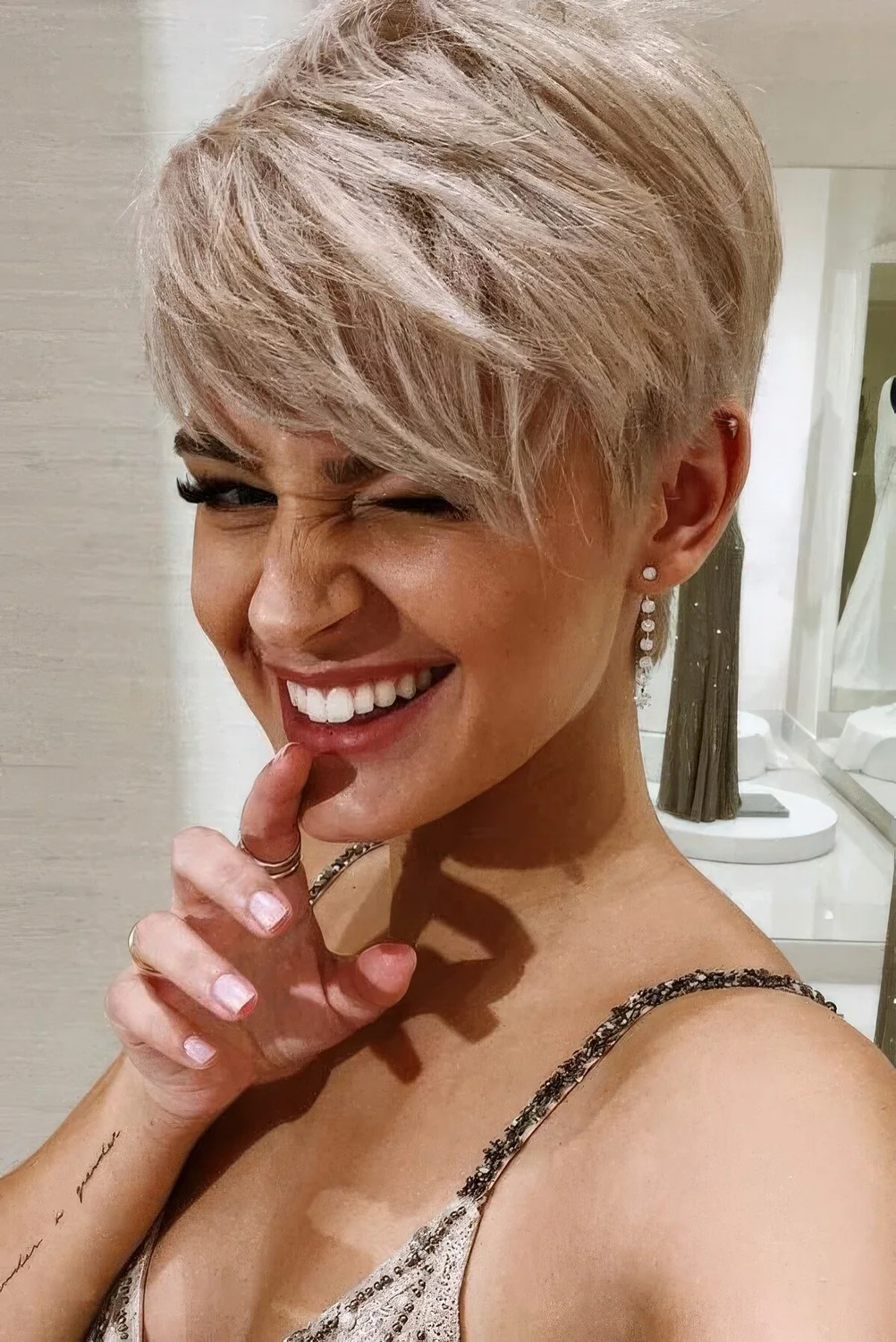 Sassy long blonde pixie cut with textured hair, side bangs and a lot of volume.