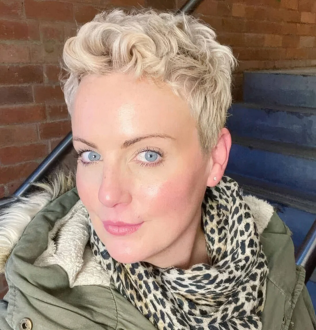 Short blonde wavy pixie haircut with some extra length on the sides and back and it.
