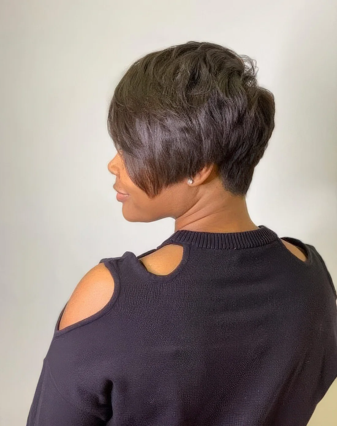 Black long pixie with long side bangs, a lot of layers and the hairline at the back that tapers into a V shape.