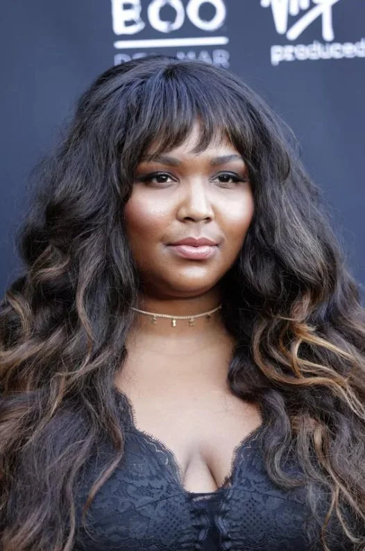 These bangs have a slight wave to them that mirrors the loose curls cascading past her shoulders, and sun kissed balayage.