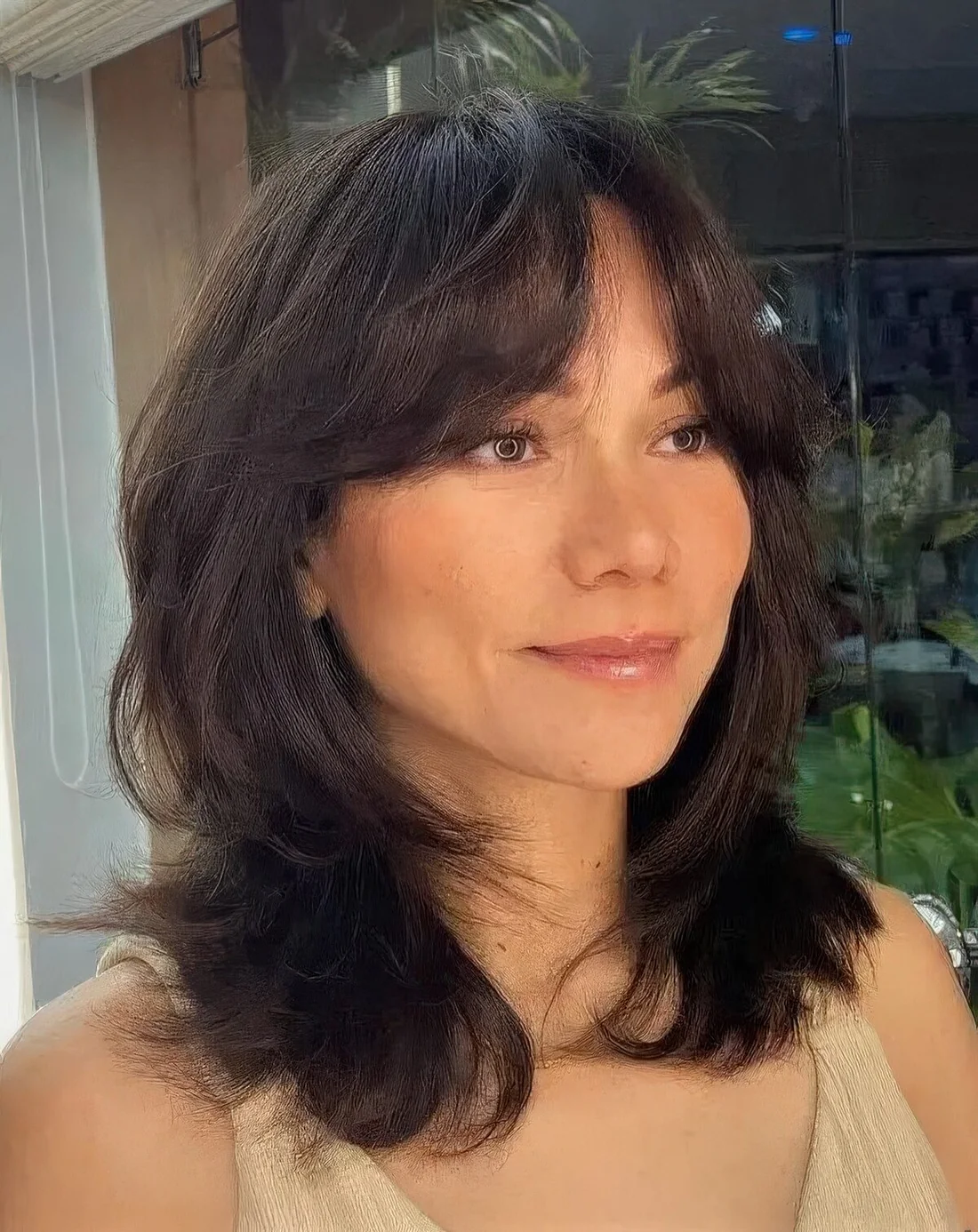Black medium-length butterfly haircut with bottleneck bangs and wavy ends.