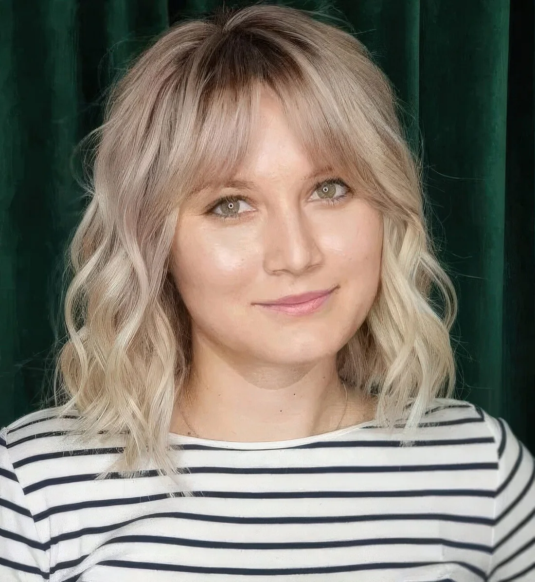 Blonde medium-length hairstyle with a darker root, bottleneck bangs and waves.