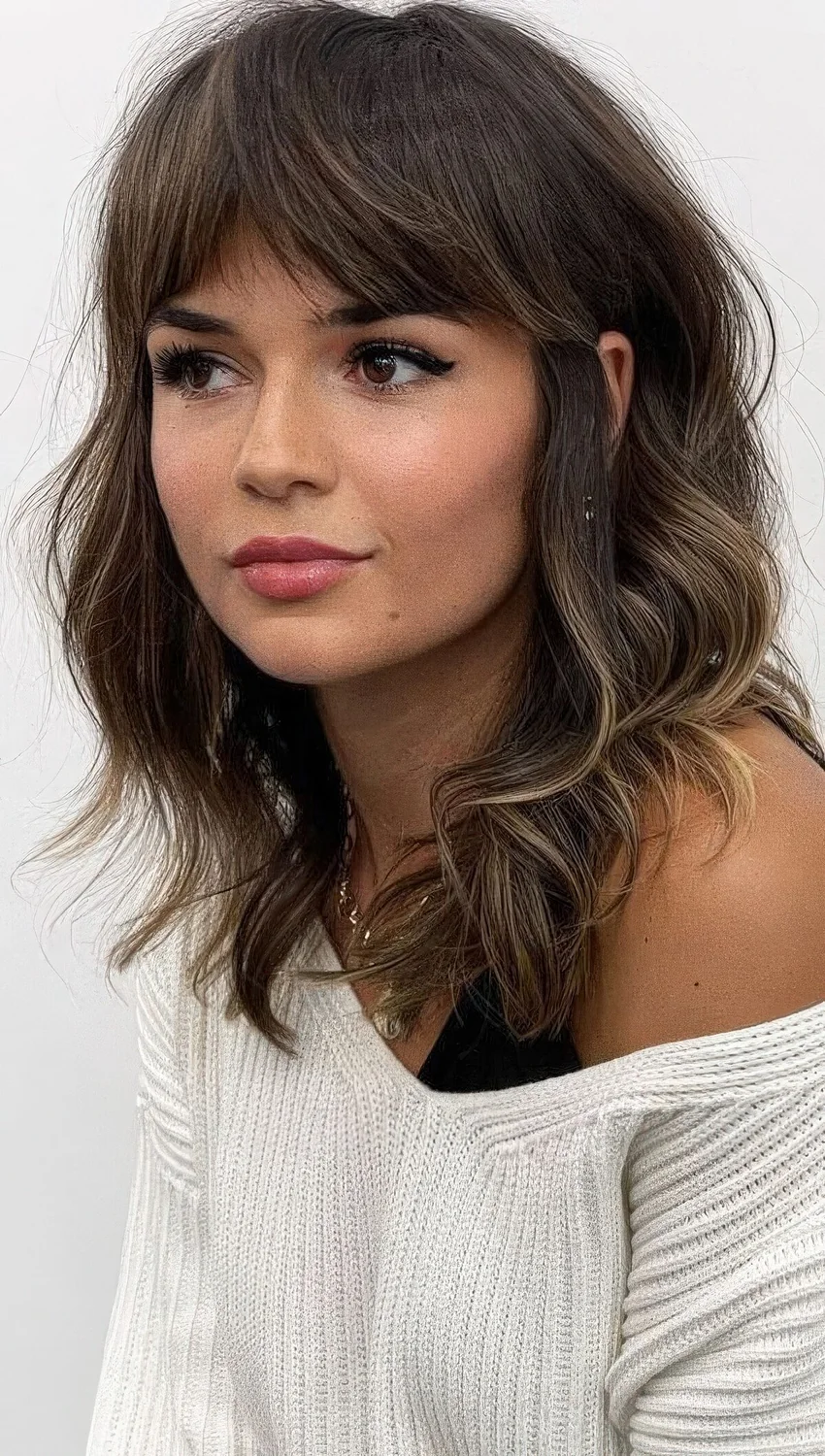 Dark brunette medium-length hairstyle with gold blonde highlights, waves and bottleneck bangs.