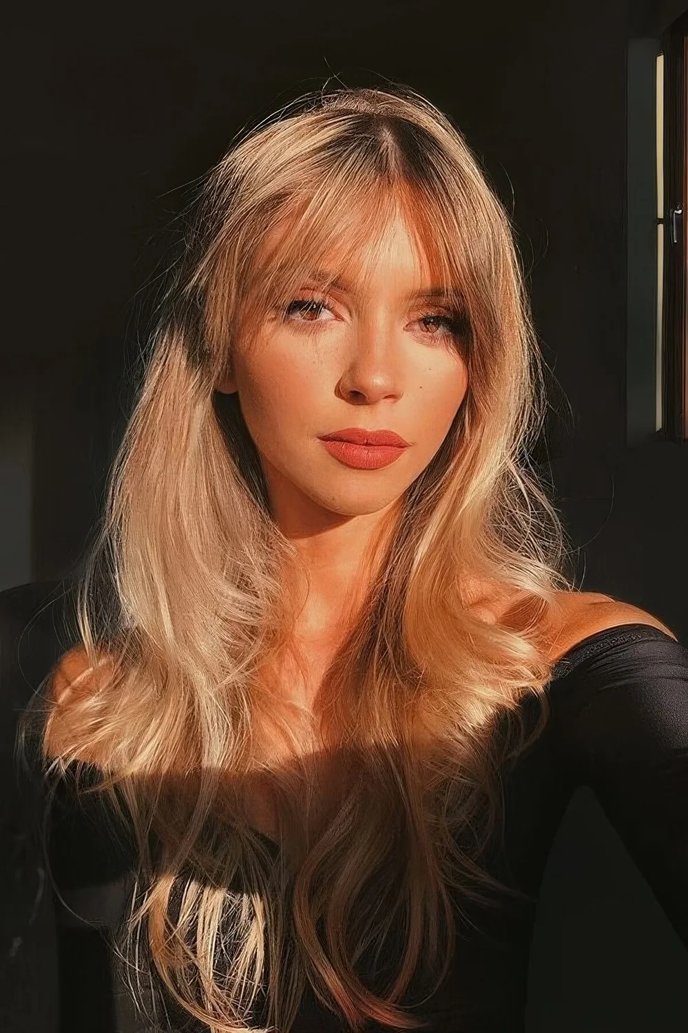 Long blonde butterfly haircut with bottleneck bangs and waves, with a bit of dimension.