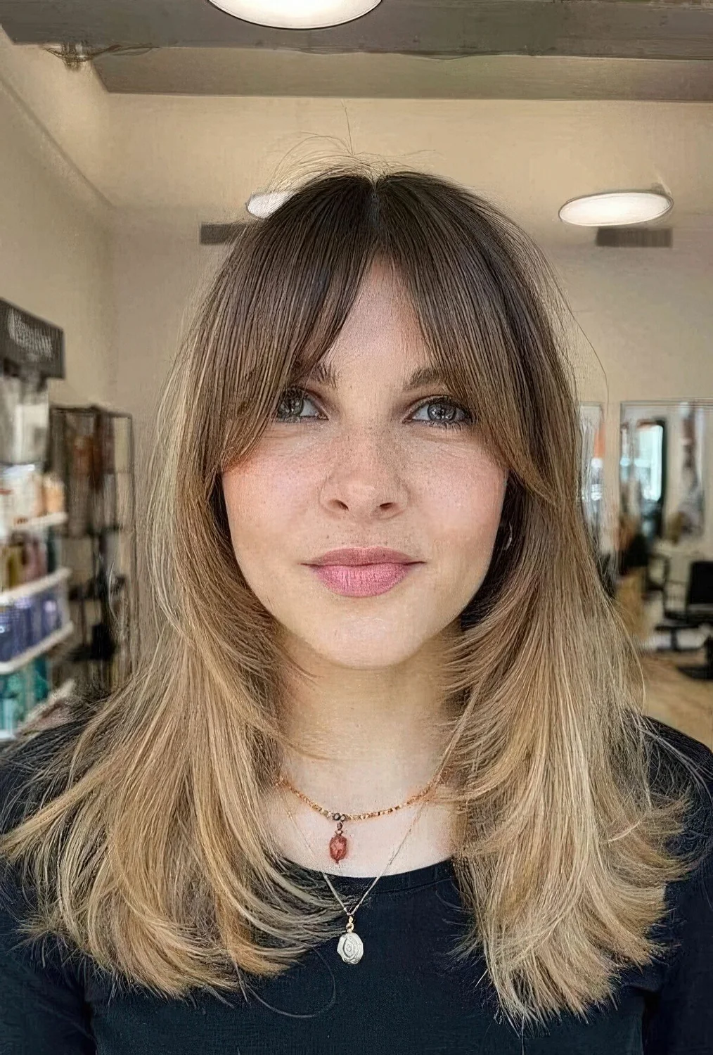 Medium blonde butterfly haircut with a darker root and front plus bottleneck bangs.
