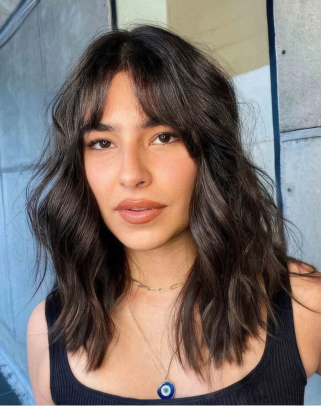 Medium-length dark brunette wavy hairstyle with bottleneck bangs and messy waves.