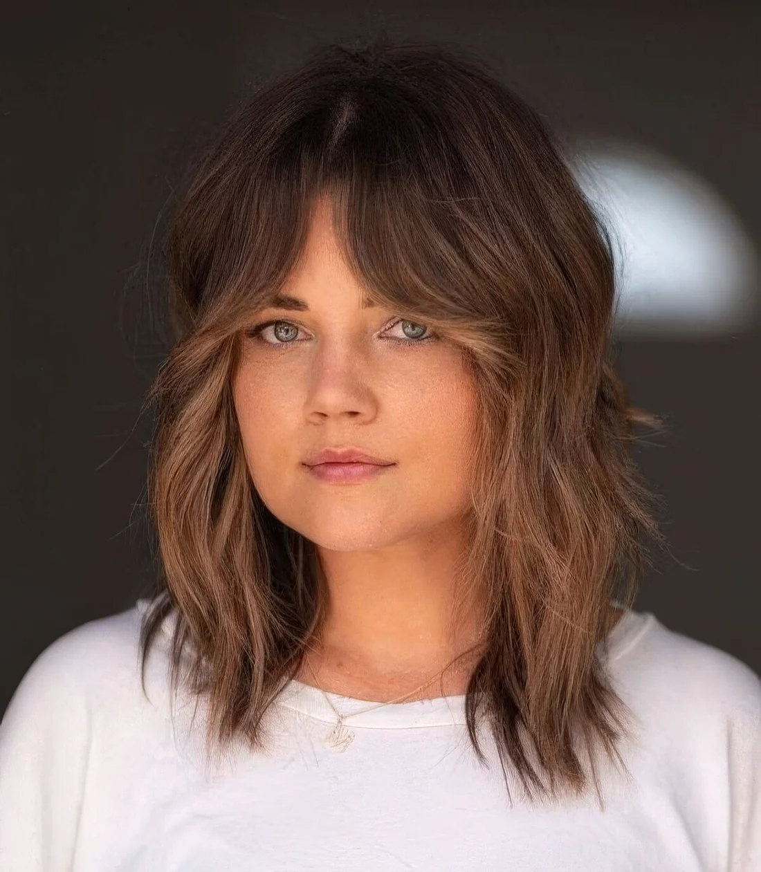 Medium-length wolf cut with caramel balayage and bottleneck bangs plus a bit of messy waves.